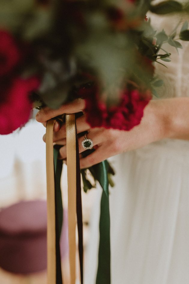 Mains d'une future mariée tenant un bouquet de rose rouge ruban vert émeraude